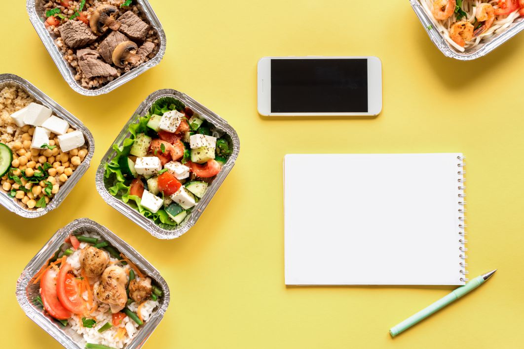 Healthy food delivery. Take away of organic daily meal on yellow, flat lay. Clean eating concept, healthy food, fitness nutrition take away in foil boxes, top view.
