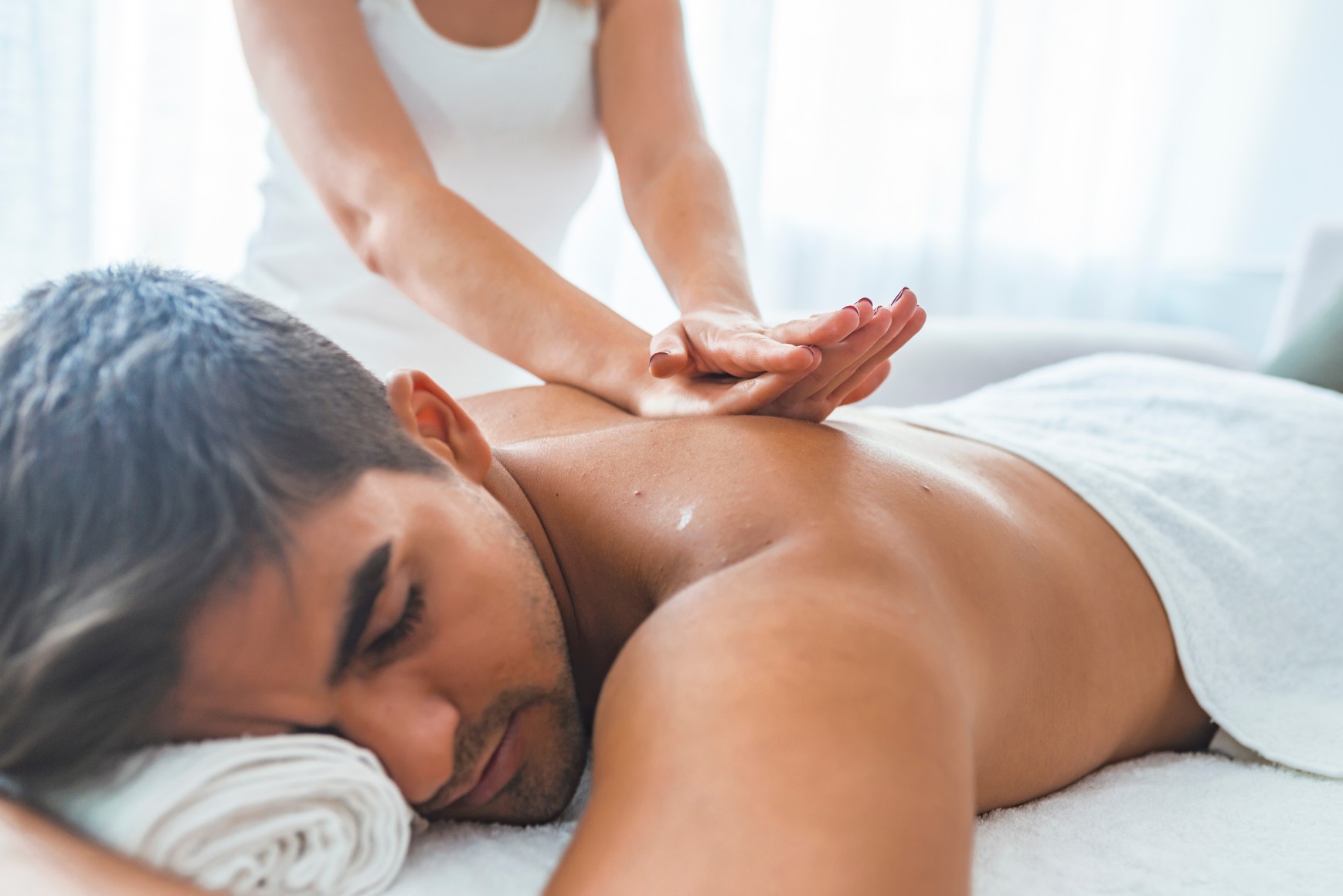 Young man is enjoying massage on spa treatment. Man having a massage in a wellness center. Handsome man receiving back massage in spa salon. Man relaxing in a wellness center